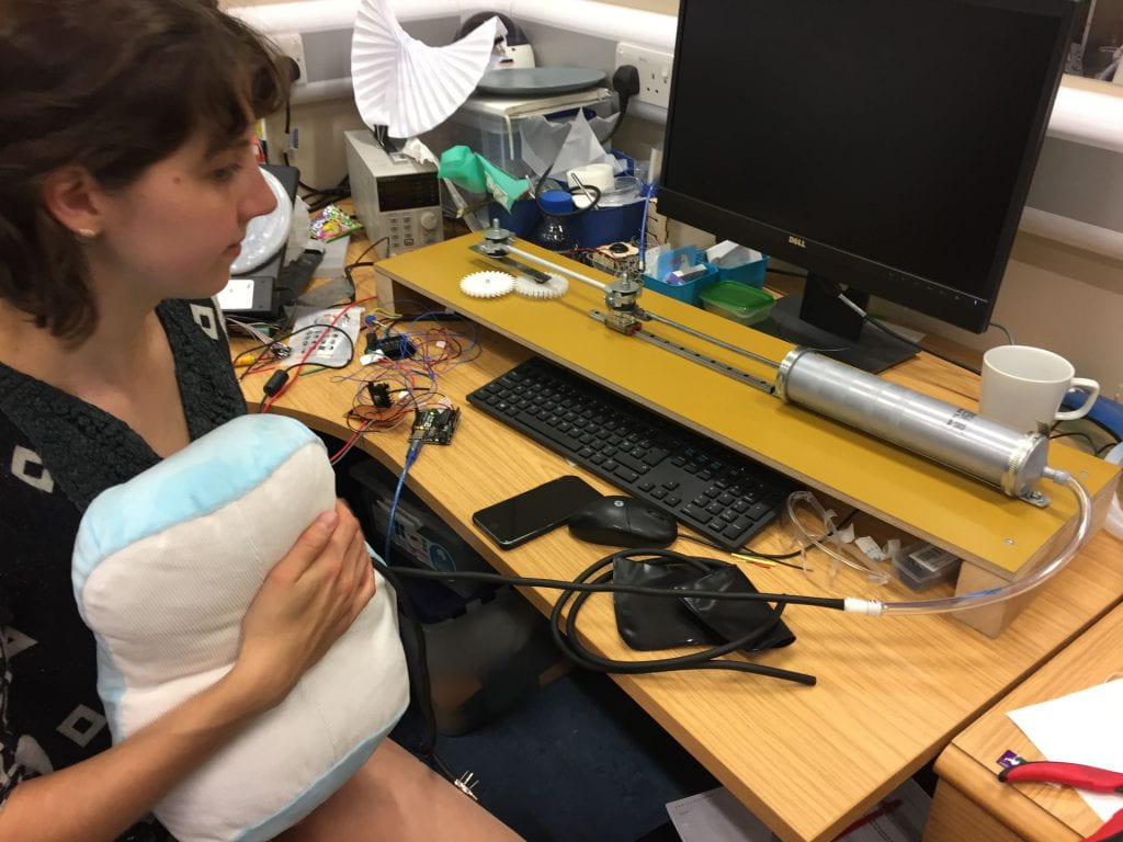 Image of a girl at a desk holding a mechanical pillow with a pump attached.