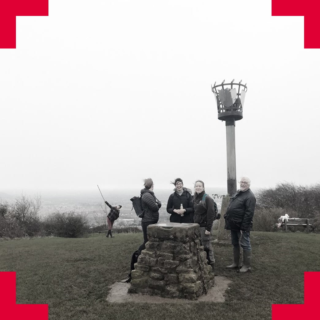 Photo of a group of people at the top of a blustry hill in front of a tall beacon