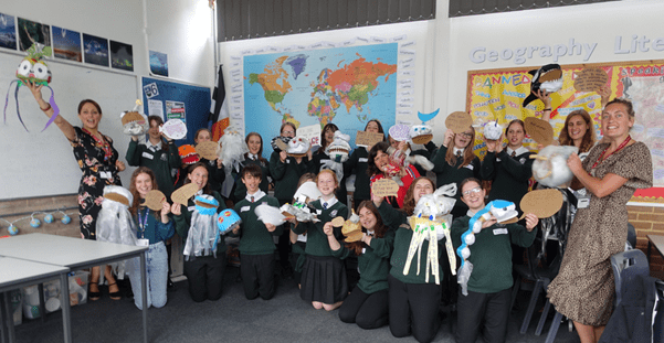 a group of children in a classroom showing their handmade animal puppets to the camera.